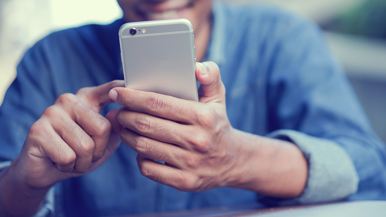 A man holding a cell phone in his hand, looking at the screen with a focused expression.